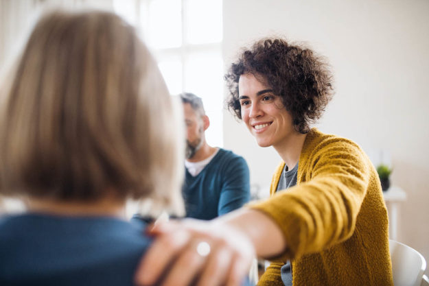 woman putting hand on another's shoulder explaining therapy options for addiction treatment